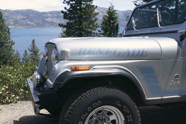 Silver Jeep with a Renegade decal by the lake